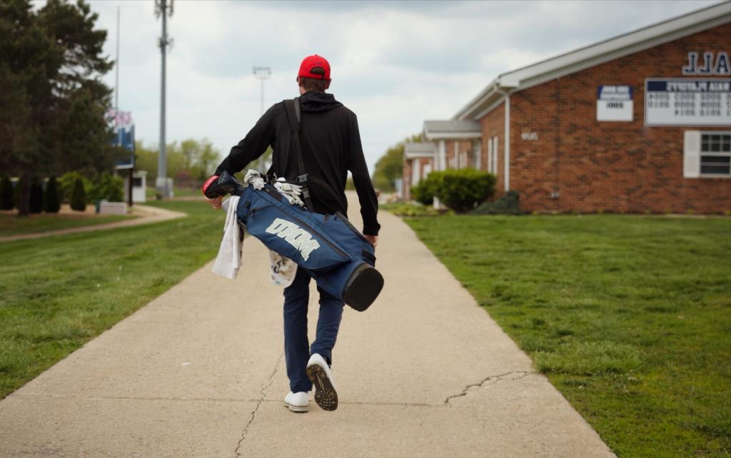 Student with golf clubs walking down a path